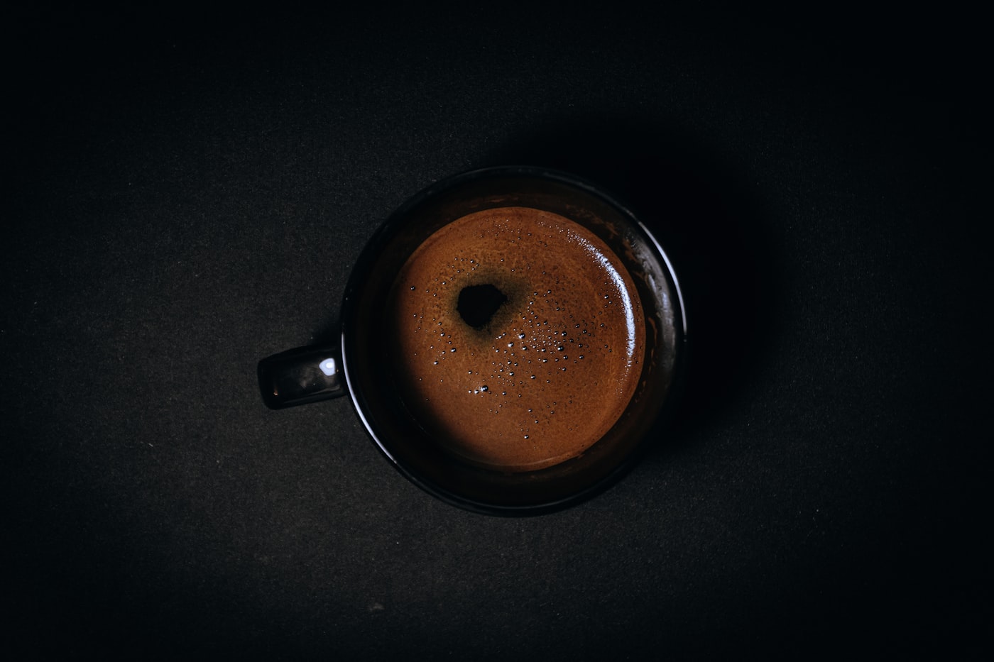 Ein frisch gezogener Espresso von oben, die Crema füllt die Tasse vor fast schwarzem Grund